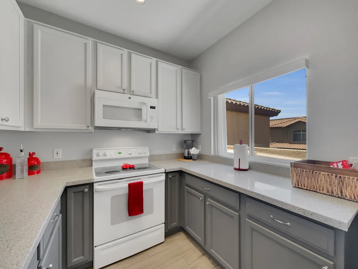 An inviting kitchen interior with a white stove, gray cabinets, and a window letting in natural light. The space looks family-friendly and functional, ideal for preparing snacks or meals to bring to the poolside or enjoy after a day outdoors.