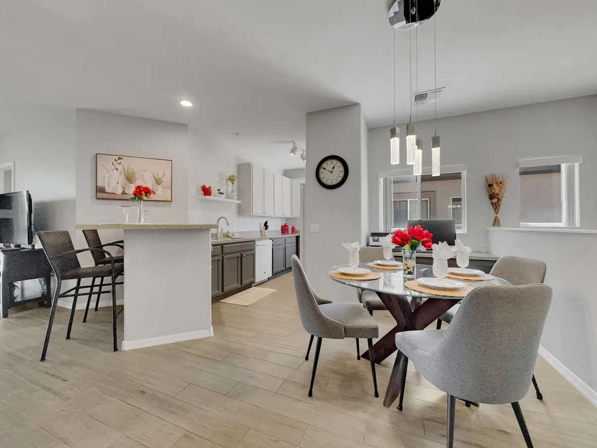 A warm and welcoming dining area features a table set with a floral centerpiece, adjacent to a modern bar area with extra seating. Stylish lighting fixtures and a spacious layout exemplify the open flow between living and dining spaces.