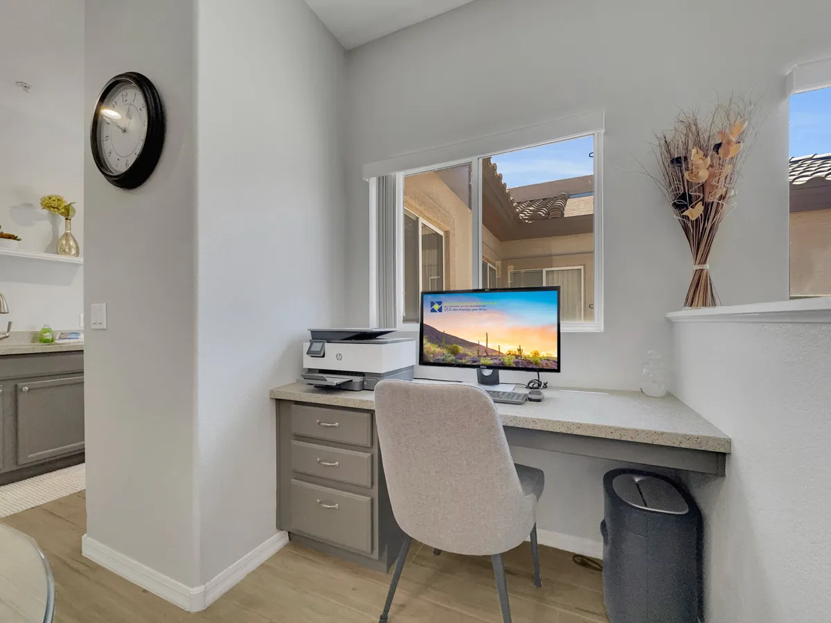 An airy interior with a desk facing a sunlit window, overlooking a green view. Decorative plants and a tidy work surface create a serene, inviting workspace—perfect for enjoying a quiet moment or productive morning with a view.