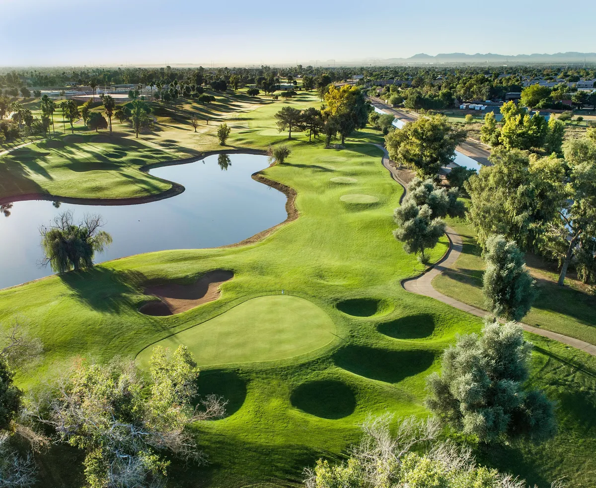 A wide view of a golf course, with a sparkling pond, mature trees, and manicured fairways. The scene is open and relaxed, inviting viewers to imagine the sweeping vistas enjoyed from their balcony. The peaceful landscape ties in elements of recreation, beauty, and exclusivity.