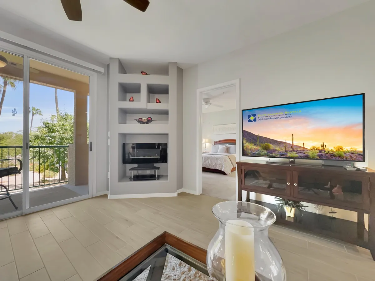 A comfortable living area featuring a glass coffee table, decorative shelving, and a balcony with expansive views. The balcony is highlighted as a perfect place to unwind and soak in the scenery, possibly overlooking the fairways.