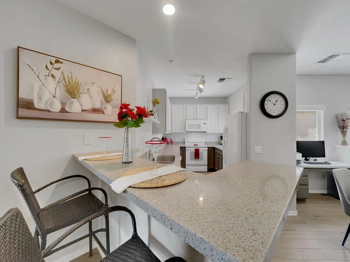 A spacious, modern kitchen with a granite countertop, sleek modern appliances, a floral arrangement, and artwork on the wall. The setting exudes an inviting atmosphere that encourages cooking, entertaining, and casual dining.