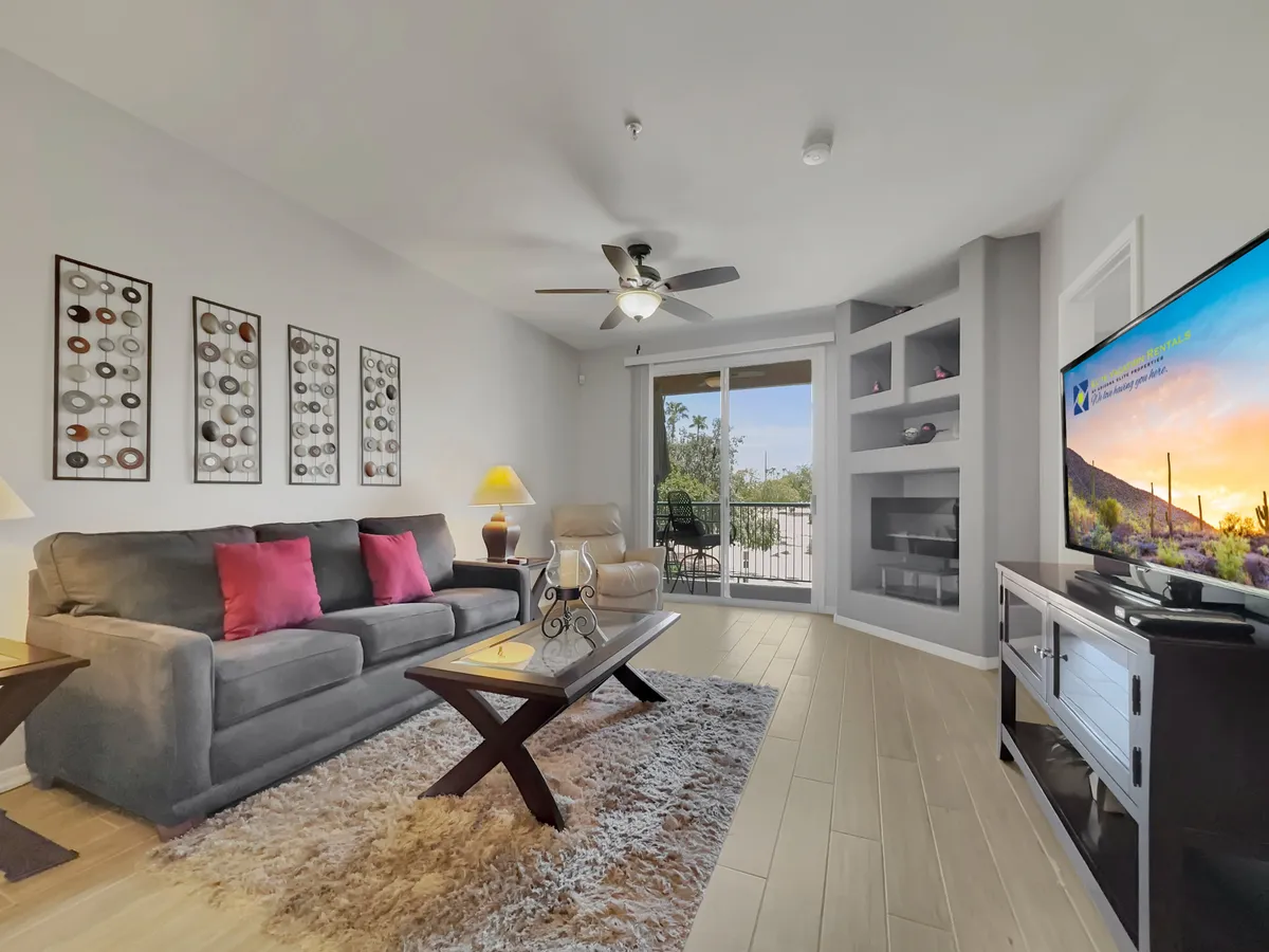 This image captures a cozy living room with a sofa adorned with pink cushions, a coffee table, a television, and a view out to the balcony. The large windows allow natural light to fill the space and offer a visual connection to the outdoors, aligning perfectly with the section’s emphasis on golf course views and plush seating.