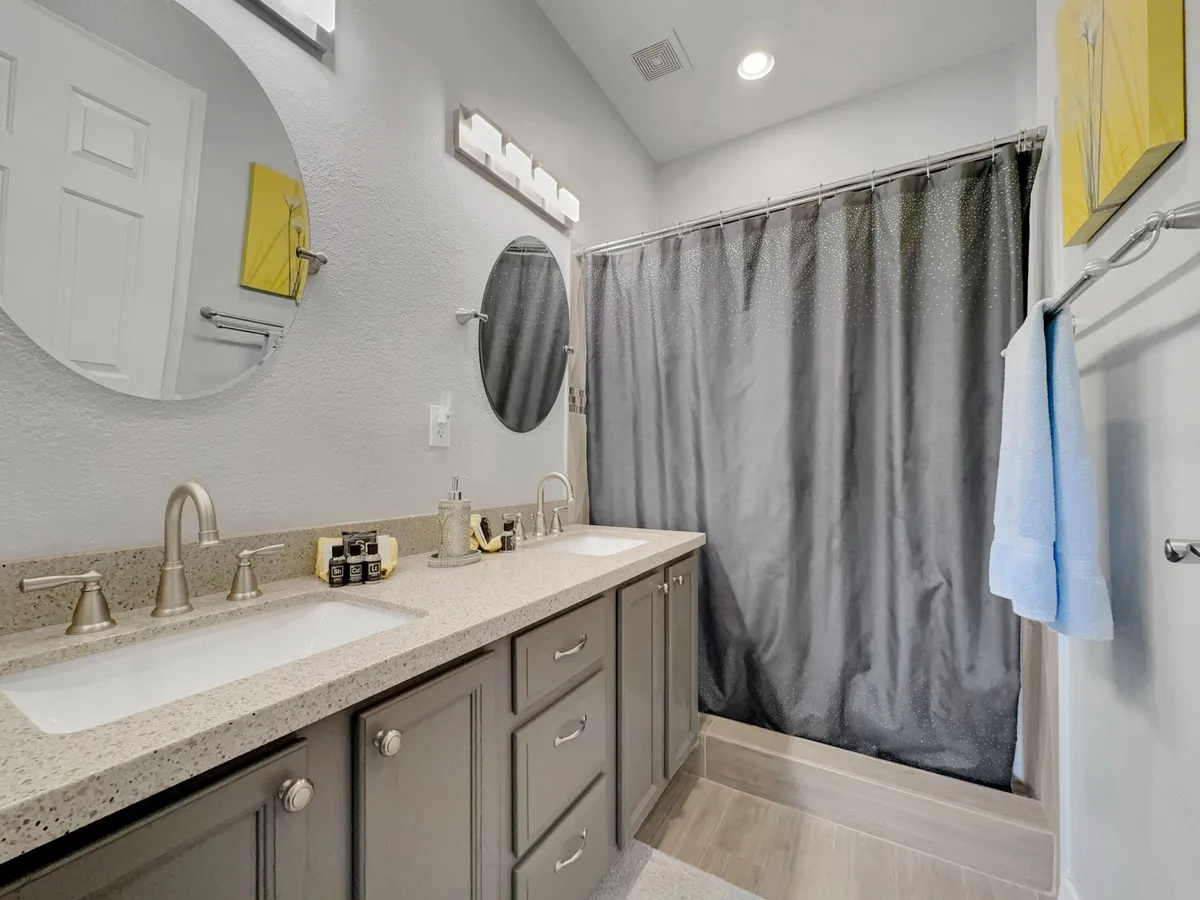 A spacious bathroom with dual sinks, mirrored cabinets, a shower curtain, and tasteful wall art. The space feels serene and inviting, designed to accommodate private morning or evening routines.
